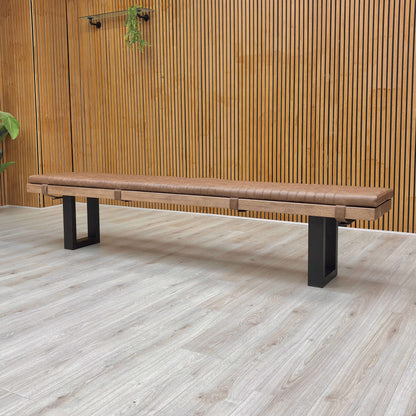 Wooden bench with black legs on a light wooden floor against a wooden wall.