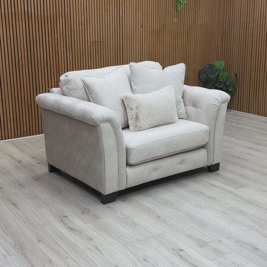 Beige fabric snuggler armchair with rolled arms and accent pillows.