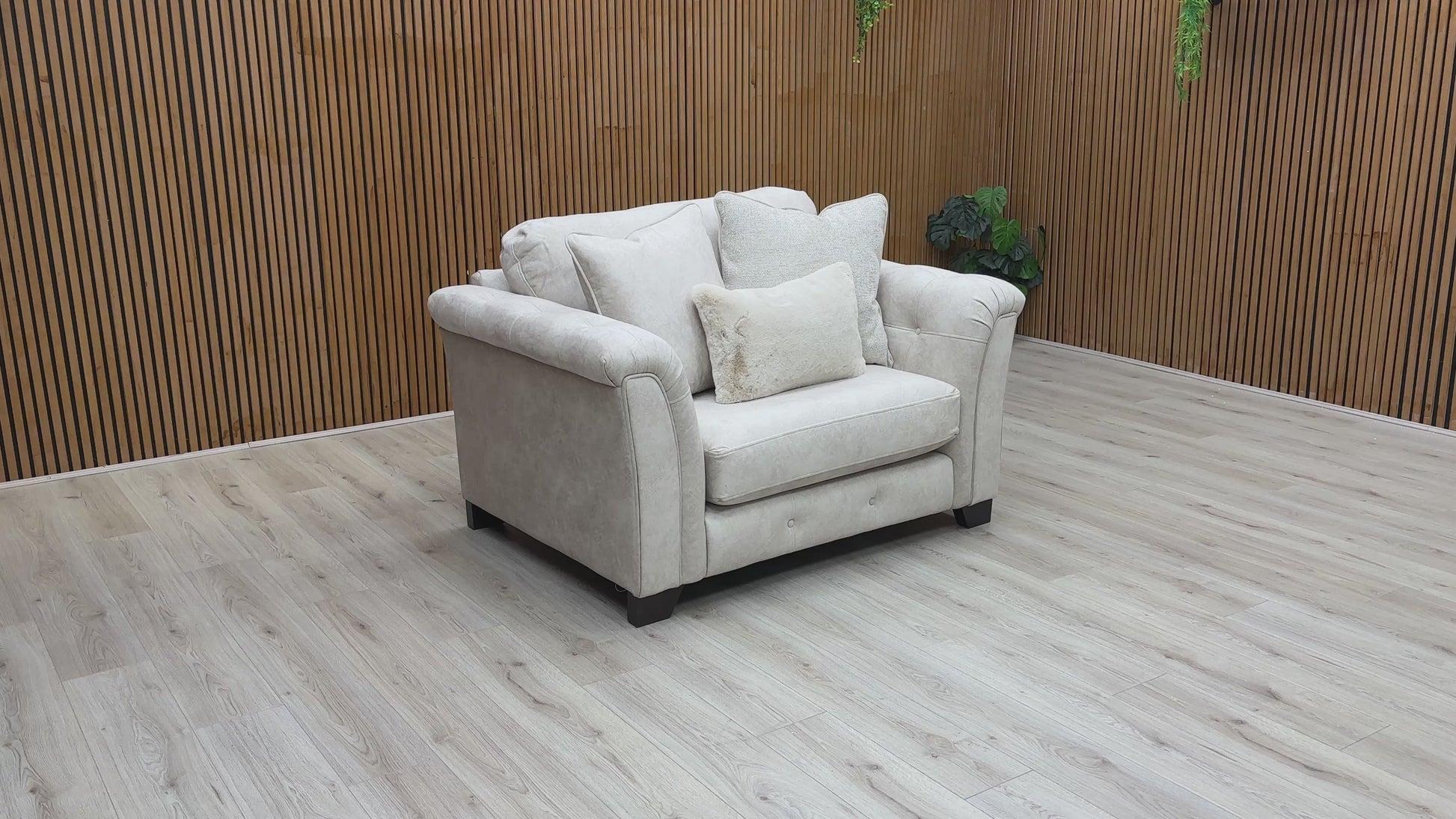 Beige fabric snuggler armchair with rolled arms and accent pillows.