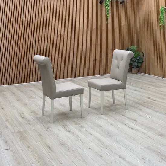 Video Of ‘Furnitureland Annecy’ dining chair set, showcasing a matching pair of two roll-back dining chairs with a soft grey painted finish and faux leather upholstery.