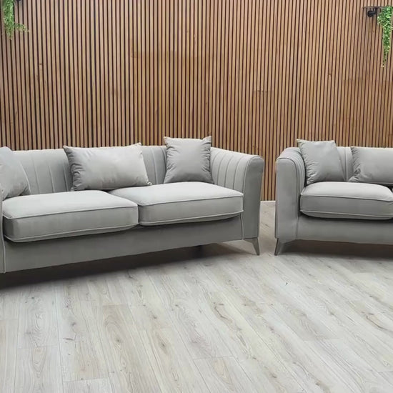 Video Of ‘Sirius’ contemporary living room furniture set, featuring a 3-seater sofa and a matching 2-seater sofa, beautifully upholstered in luxurious Pebble Grey velveteen fabric with a classic back design.