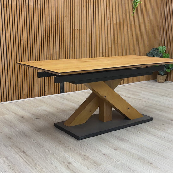 A video of a Wooden dining table with a black base against a wooden wall.