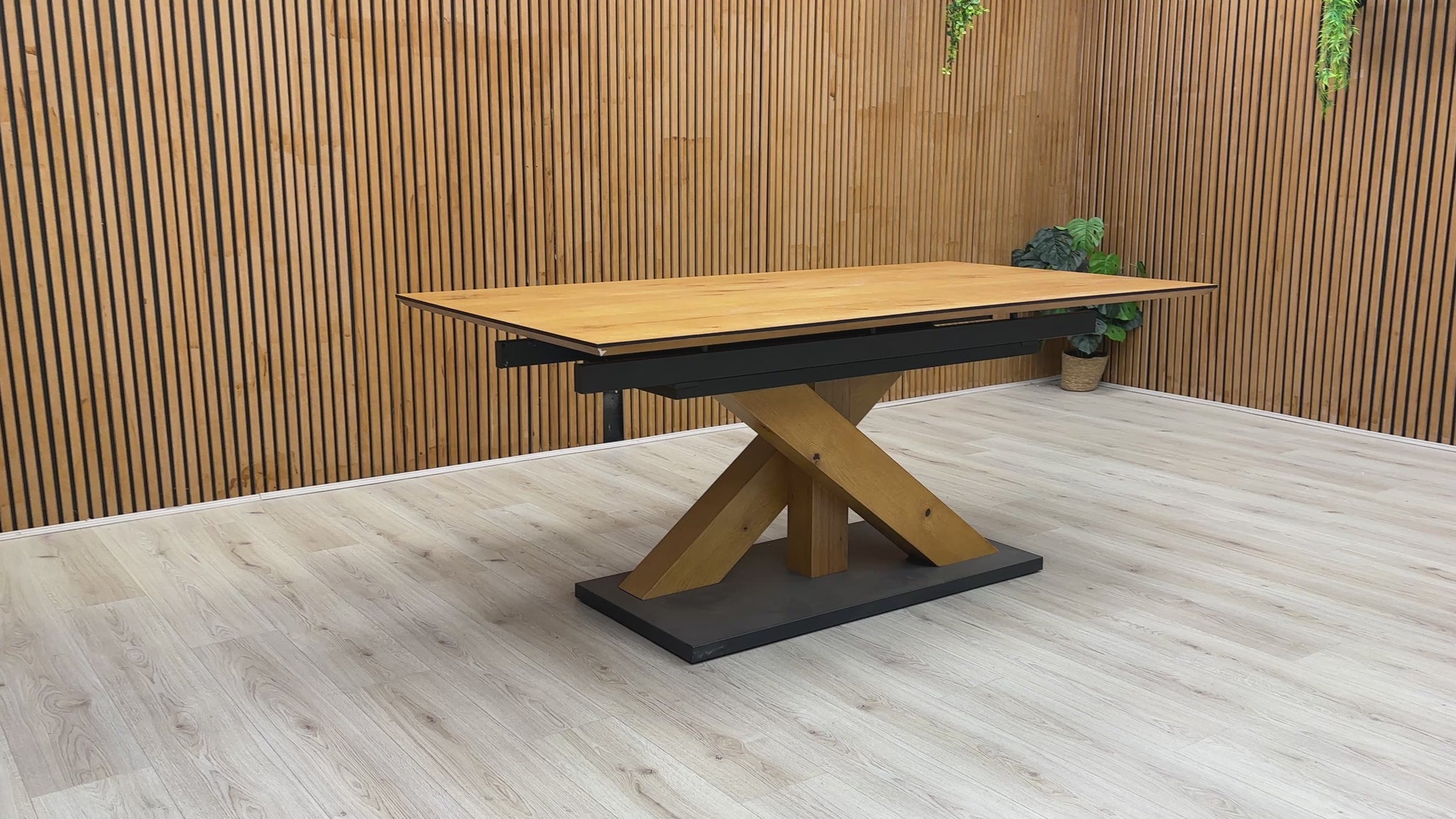 A video of a Wooden dining table with a black base against a wooden wall.
