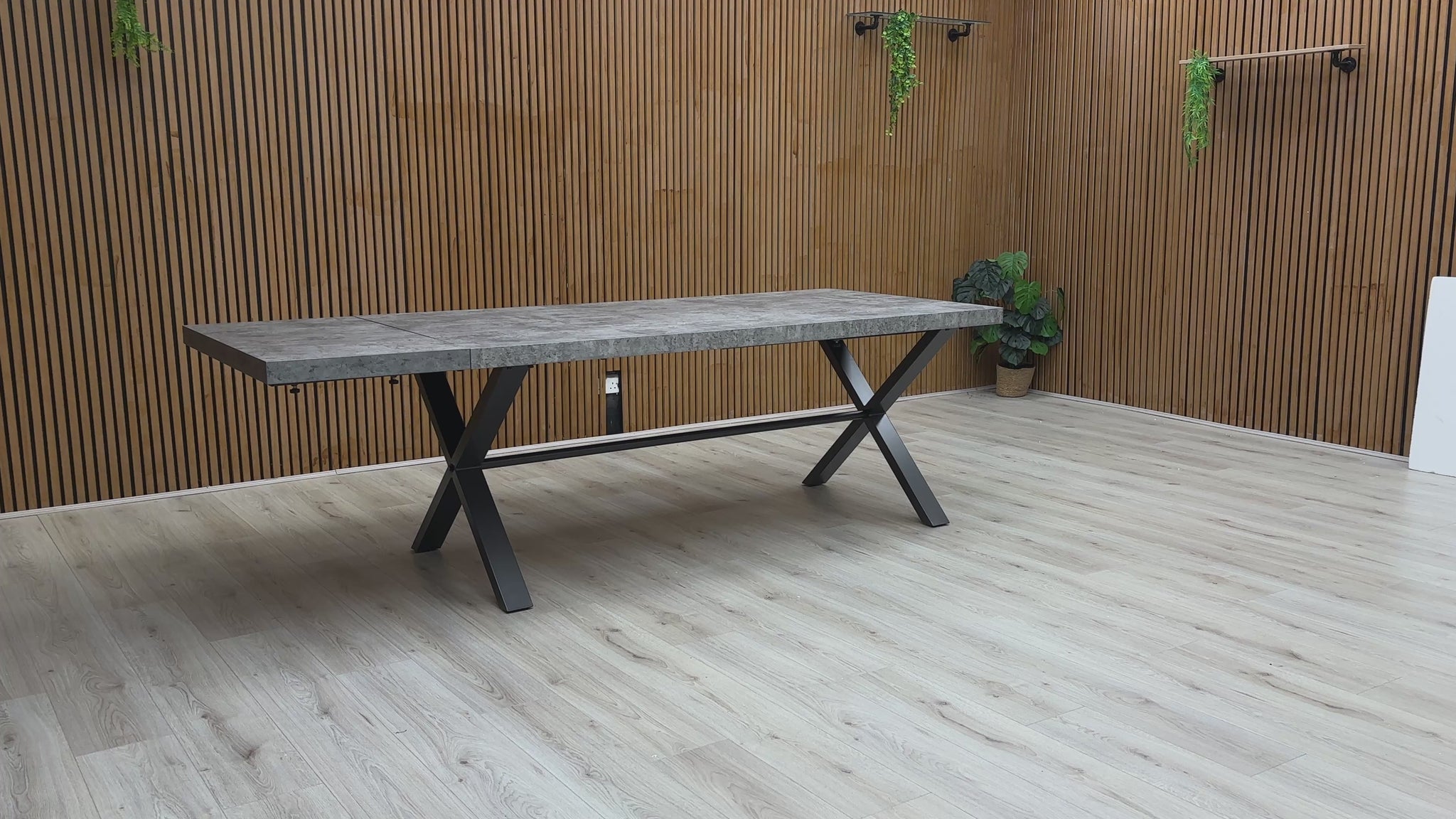 A video of Long rectangular table with a concrete top and black metal legs against a wooden wall.