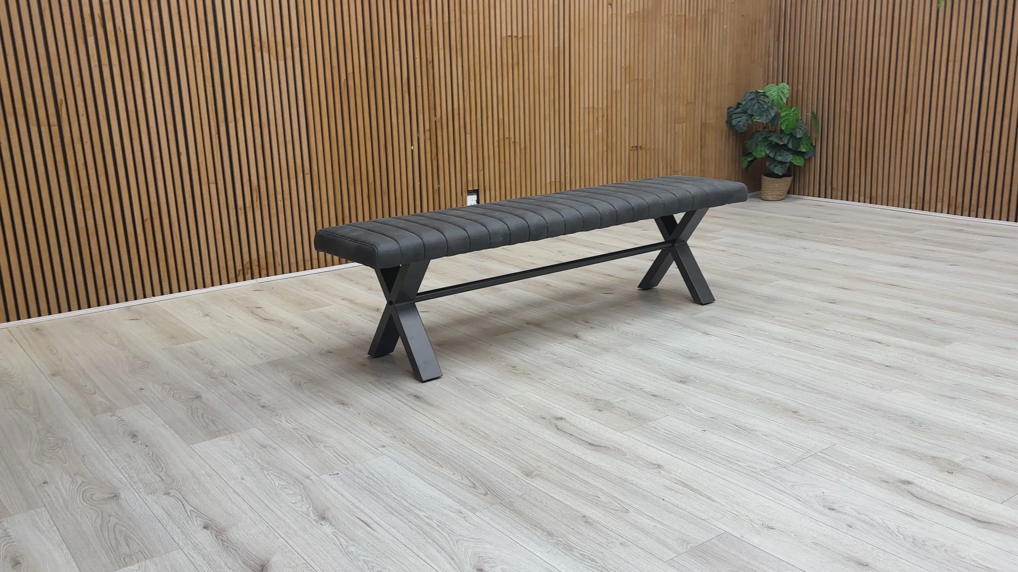 A video of Gray bench with X-shaped legs on a wooden floor against a wooden wall.