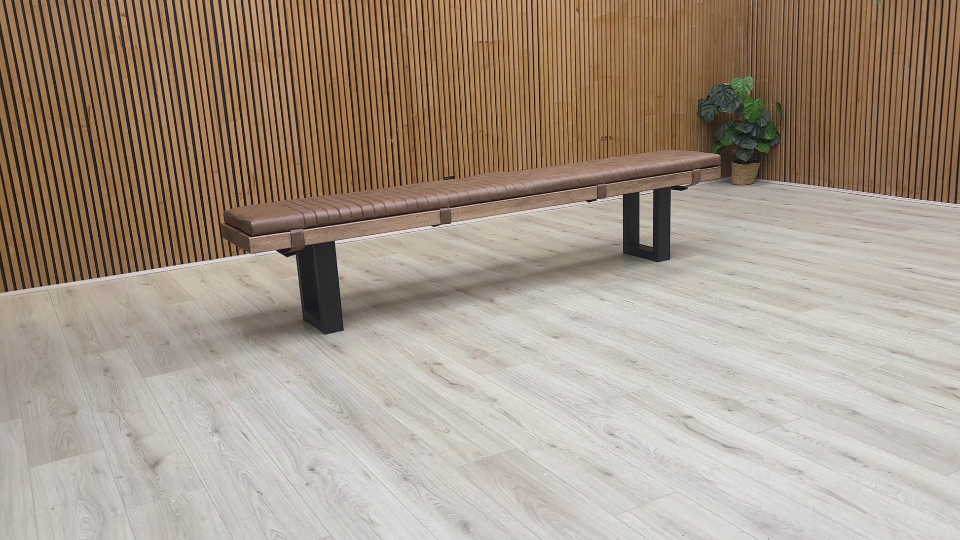 A video of Wooden bench with black legs on a light wooden floor against a wooden wall.