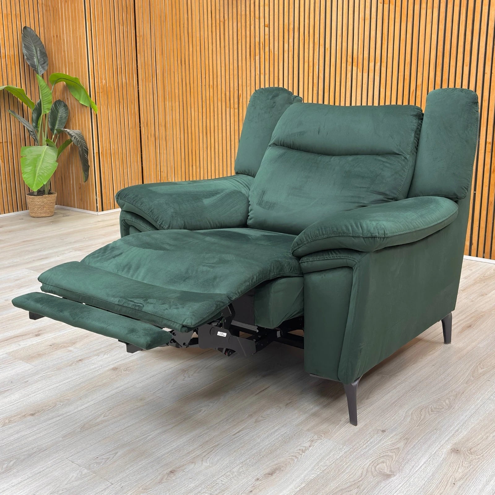 Lifestyle shot of the bottle green velvet recliner armchair highlighting the sleek open-base design and metal legs.