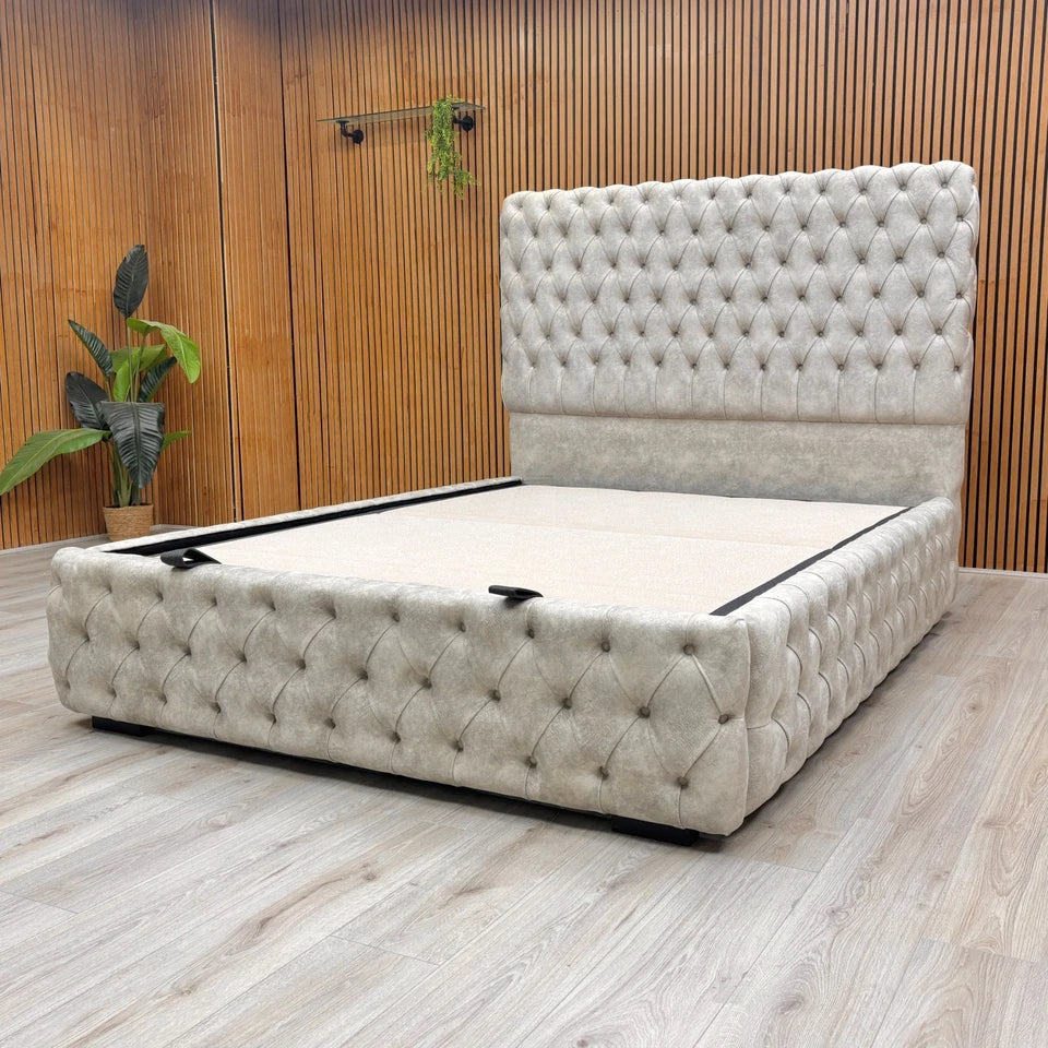 Belford Dapple Oyster Velvet King Size Bed with a tall, floor-standing headboard and end-lift ottoman storage, styled with decorative pillows across a wooden background