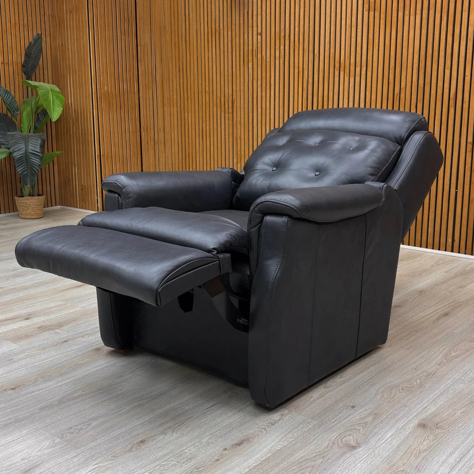 Black leather recliner chair in a room with wooden walls and a plant.