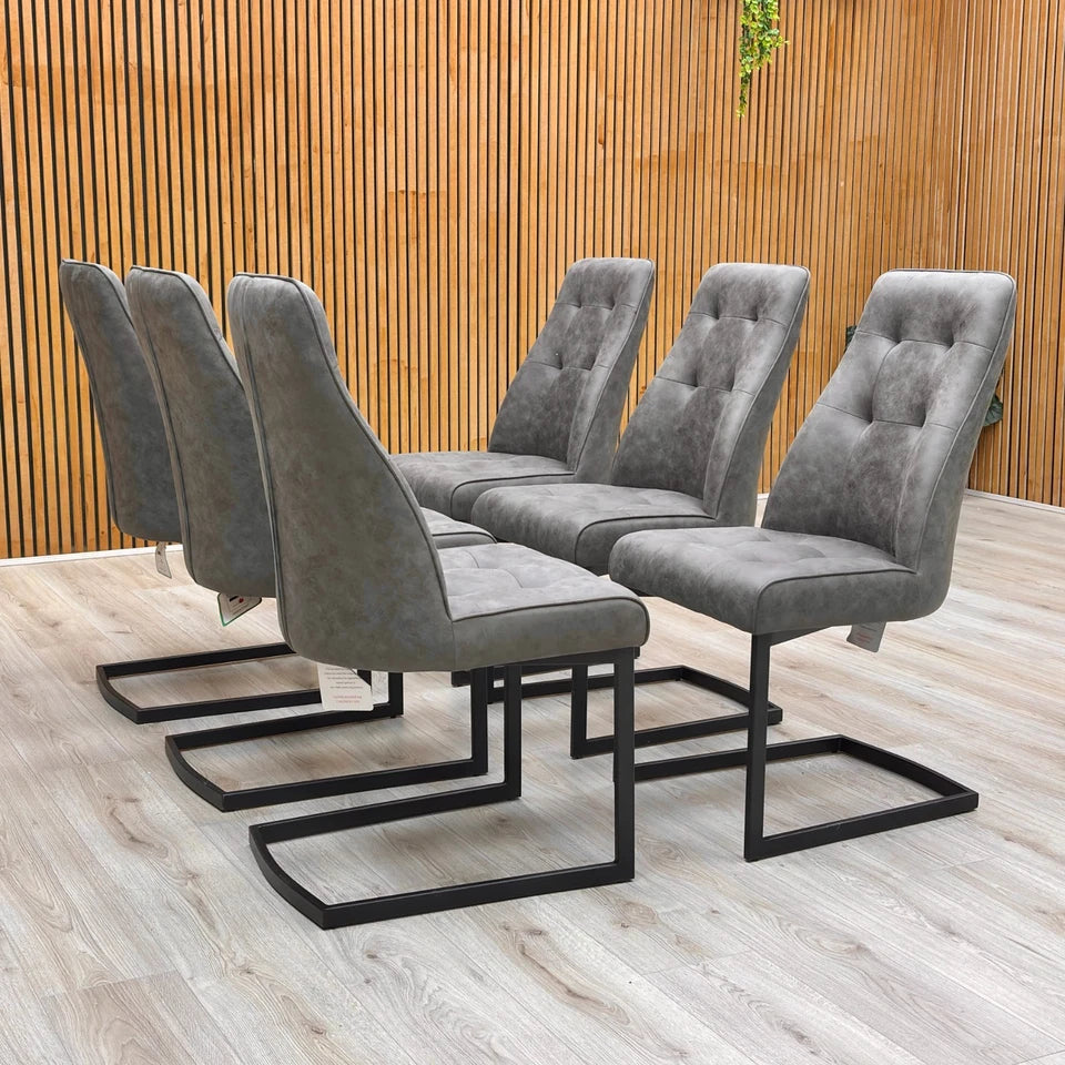 Lifestyle view of a Merlin charcoal grey suede dining chairs showing the C-shaped cantilever chrome frame.
