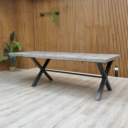 Long rectangular table with a concrete top and black metal legs against a wooden wall.
