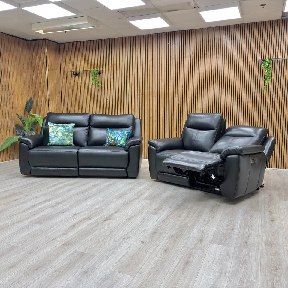 Black leather sofa and recliner chair in a room with wooden walls and ceiling lights.