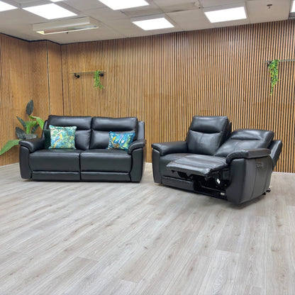 Black leather sofa and recliner chair in a room with wooden walls and ceiling lights.