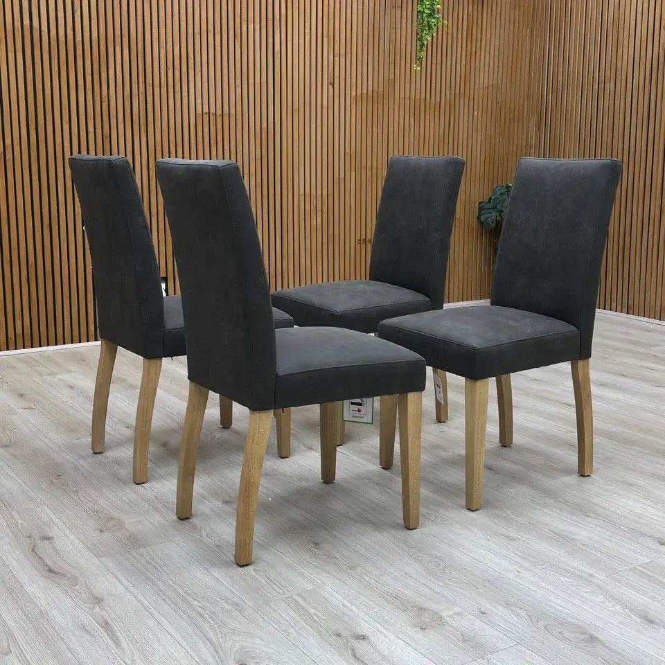 Four dark gray chairs with wooden legs on a wooden floor.