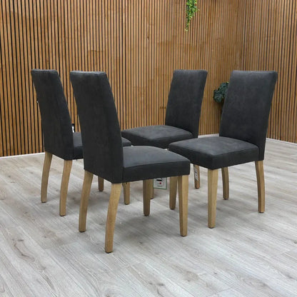 Four dark gray chairs with wooden legs on a wooden floor.