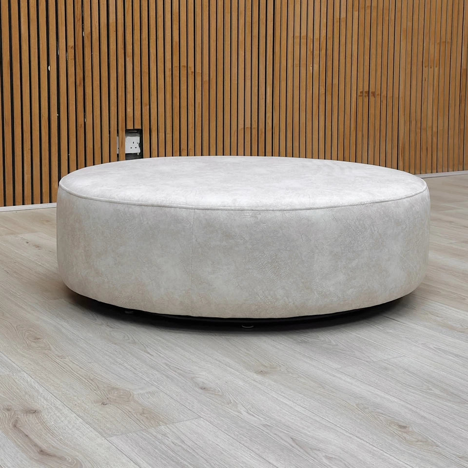 The Mariah twister footstool placed in a room setting, showing the creamy color and velvet-like texture of the nubuck leather-look base