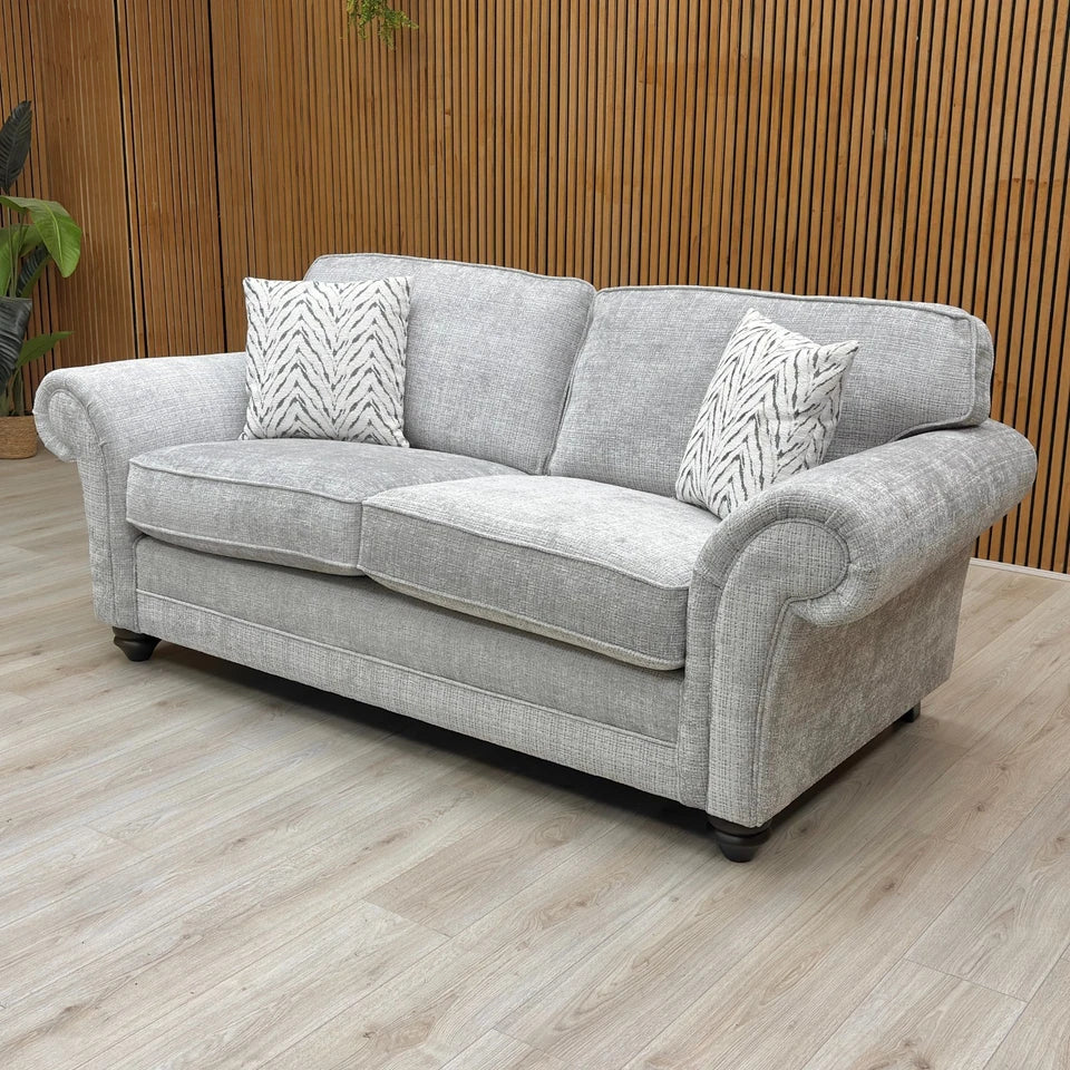 An angled side view of the sofa, highlighting the texture of the silver woven fabric and the shape of the elegant scroll armrests.