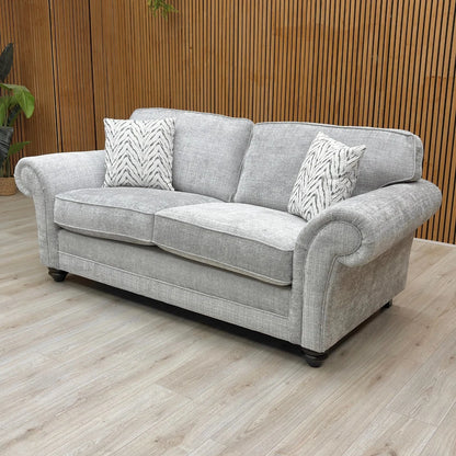 An angled side view of the sofa, highlighting the texture of the silver woven fabric and the shape of the elegant scroll armrests.