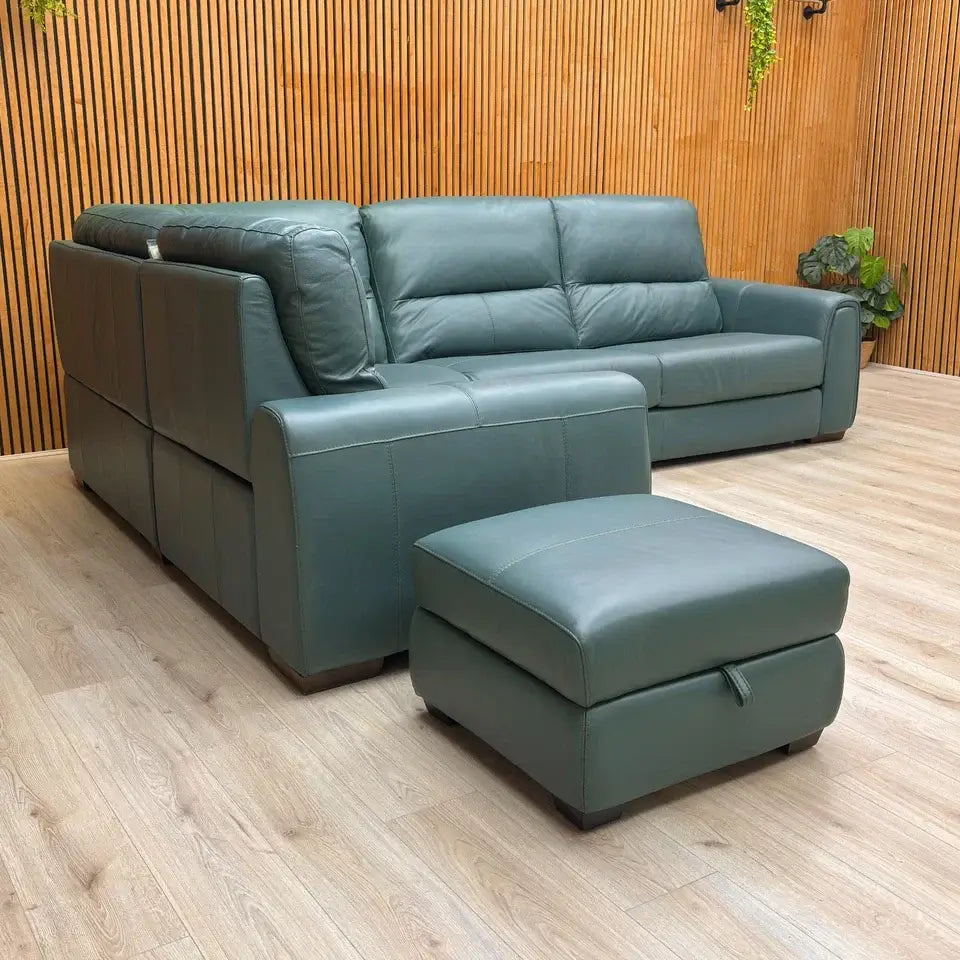 Green leather sectional sofa with ottoman on a wooden floor against a wooden wall.