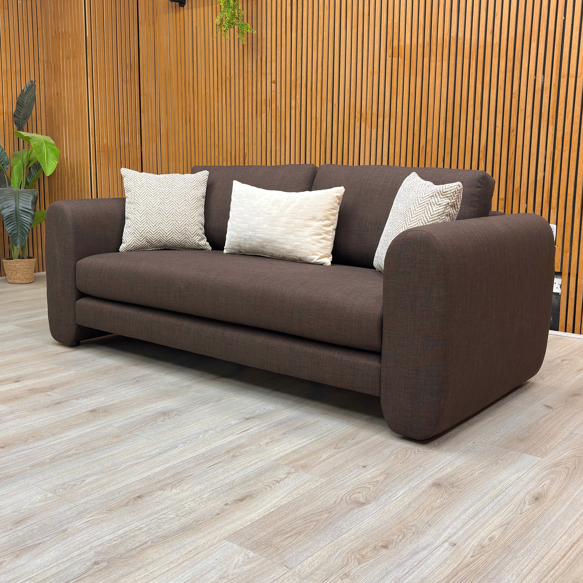 Brown sofa with white pillows in a room with wooden walls and floor.
