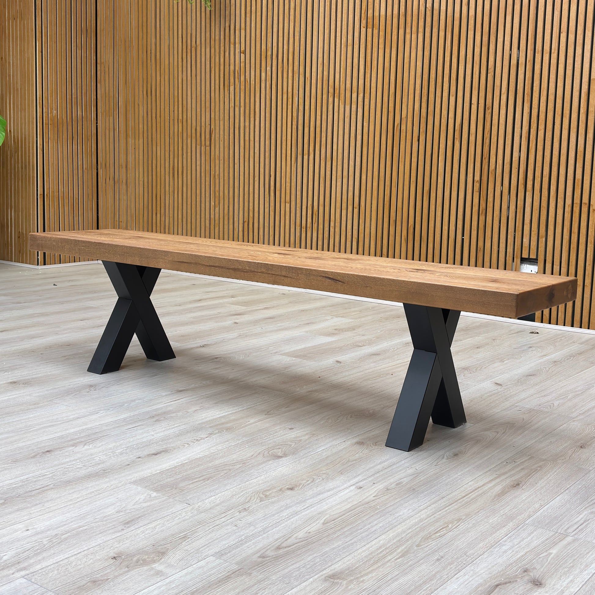 Detailed view of the metal X-shaped legs of the Njord dining bench, contrasting the dark metal with the light wood.